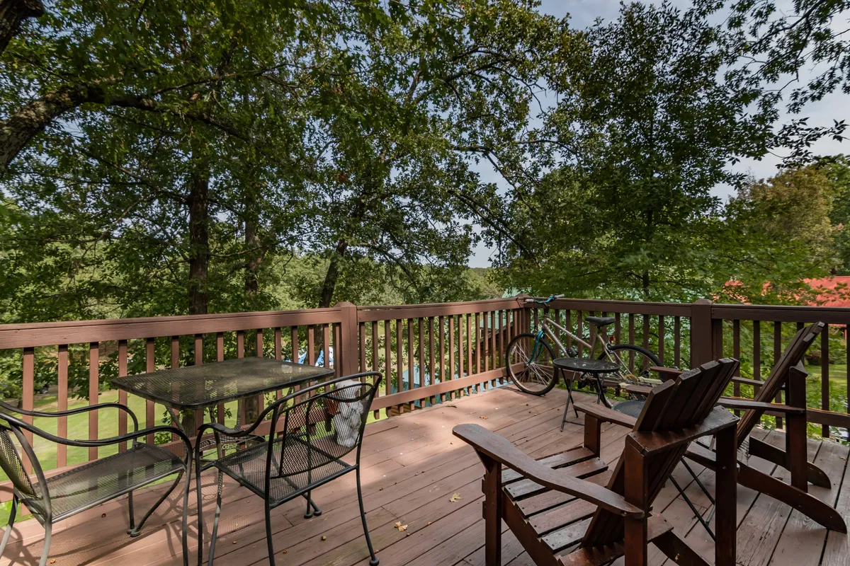 A peaceful wooden deck furnished with outdoor seating and a stationary bike, surrounded by trees. The area invites relaxation, exercise, and moments spent observing wildlife or the night sky.
