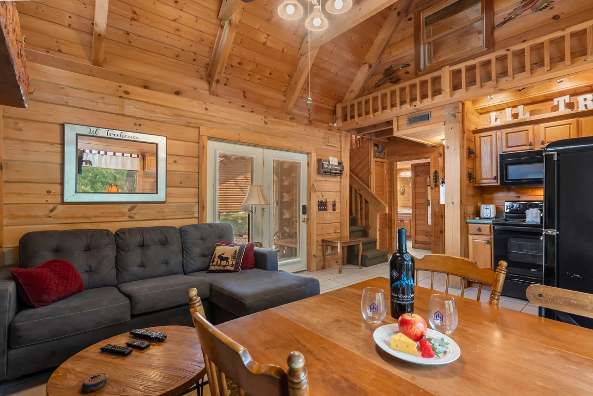 An open-plan dining area with a rustic wooden ceiling, a dining table set with wine and fruit, a comfortable sofa, and a clear view of the adjoining kitchen. The scene radiates warmth and togetherness, with space for both dining and socializing.