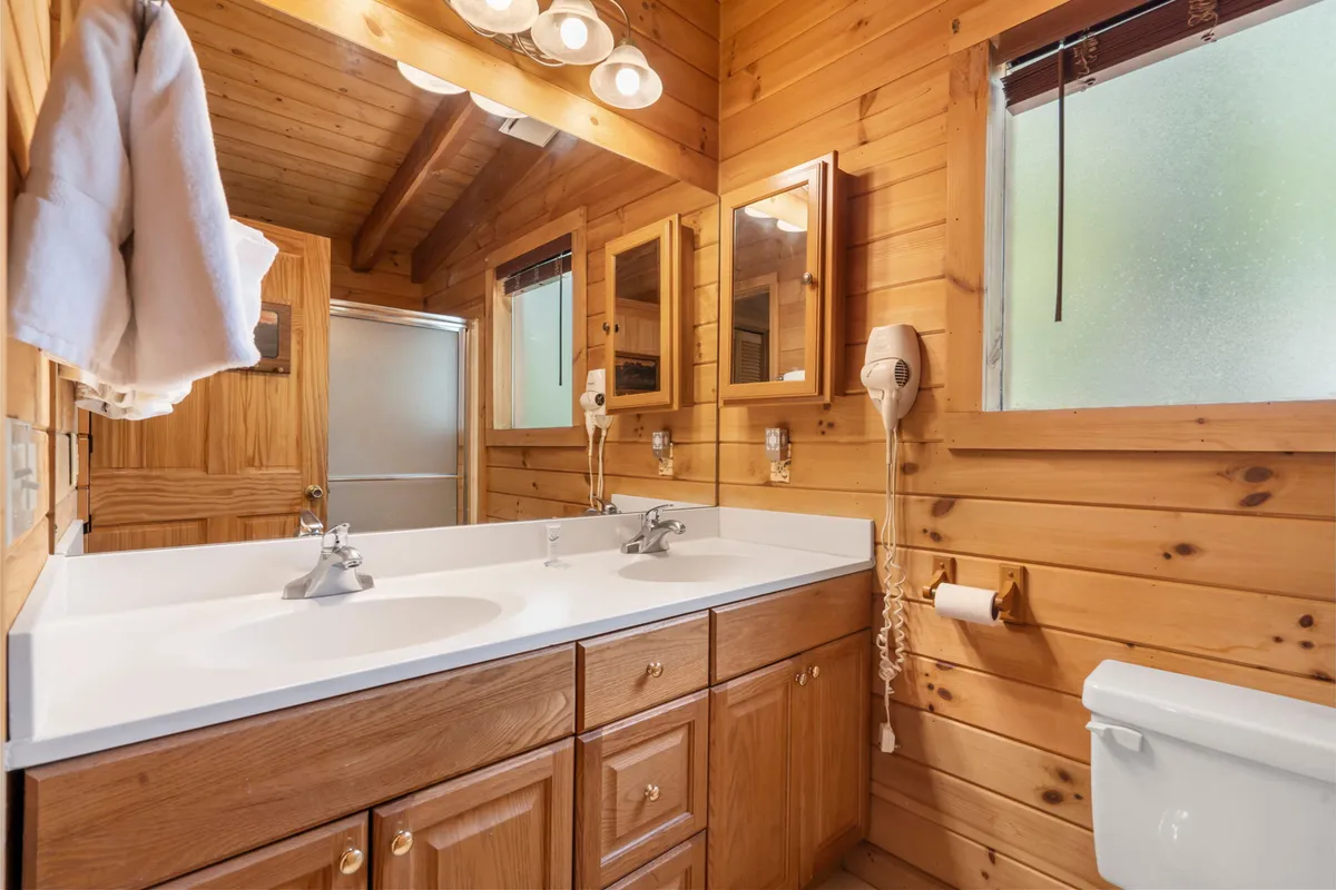 A spacious bathroom with dual sinks, wooden cabinetry, large mirrors, and stylish light fixtures. The design exudes warmth and tranquility, perfect for self-care routines and spa-like relaxation.