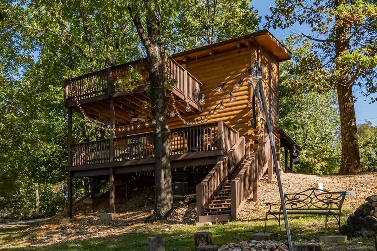 A cozy wooden cabin nestled among trees, showcasing multiple private decks and an outdoor seating area. The decks offer ample space for relaxation or spending quality time outdoors, while the surrounding trees provide shade and a sense of privacy.