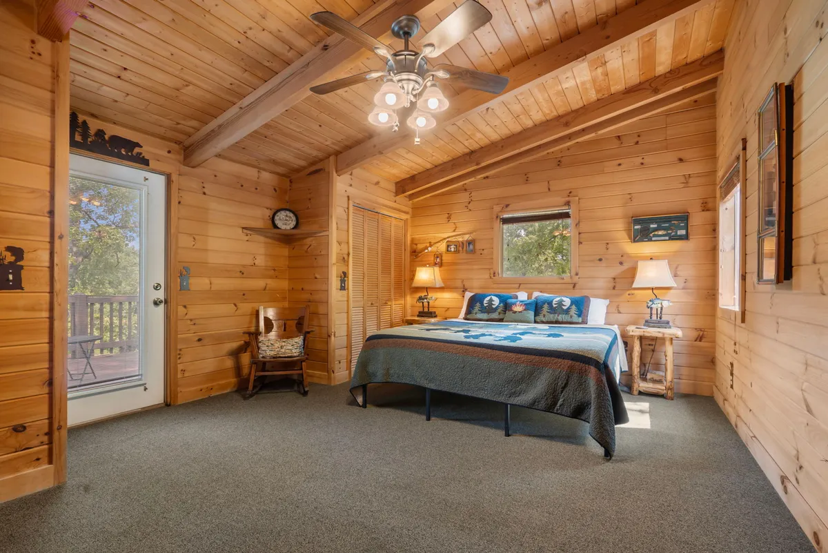 An inviting bedroom with a comfortable bed, wooden ceiling, multiple windows allowing nature views, and ambient table lamps. The soft lighting and window placement foster a tranquil escape for sleep and relaxation.