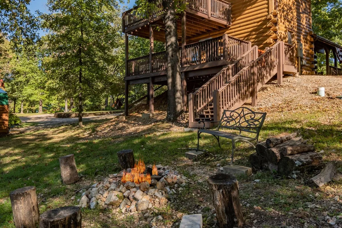 A cozy fire pit area nestled among trees, with a bench and wooden stairs leading down from the deck. The intimate setup is perfect for evenings spent sharing stories and roasting s’mores under the stars.