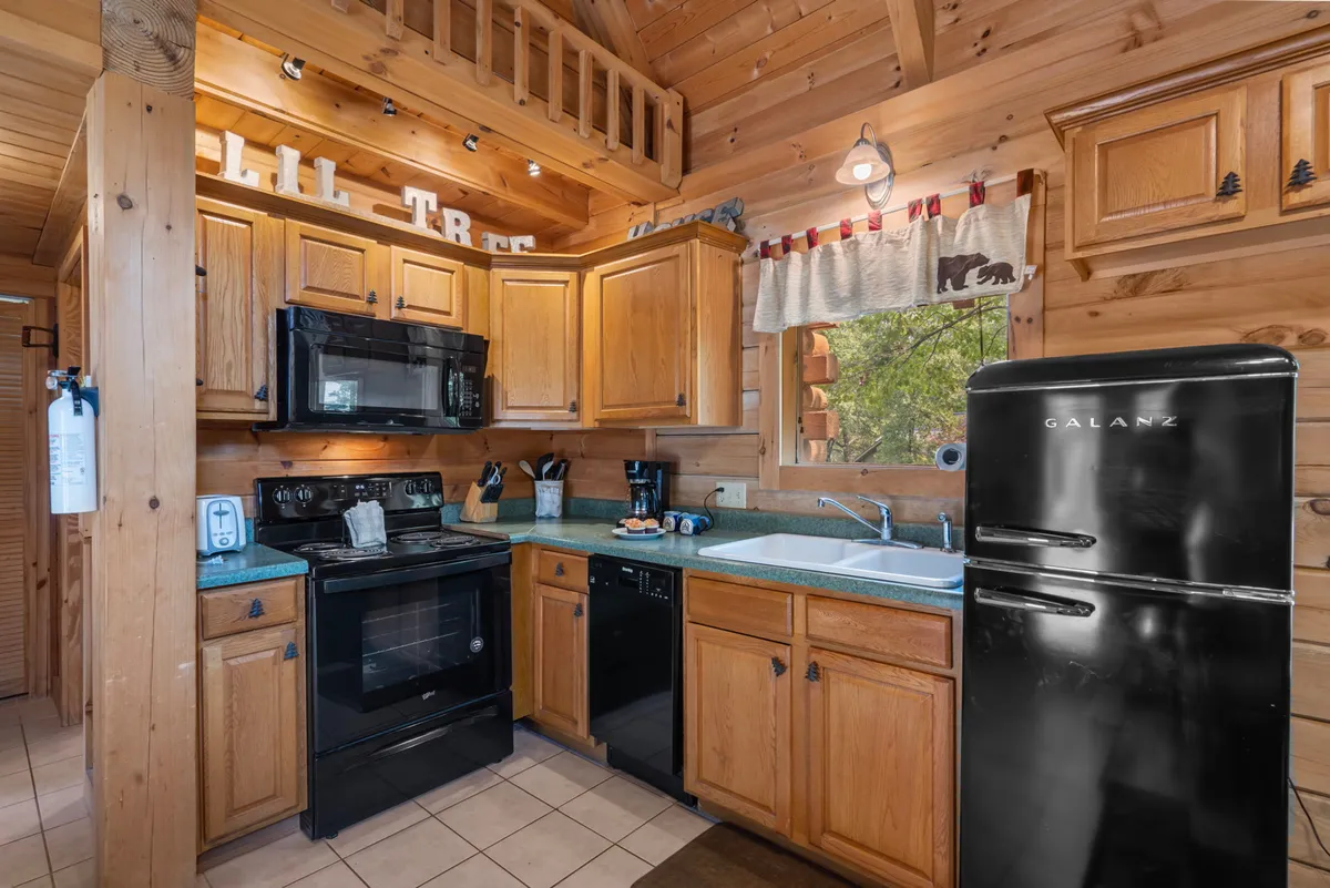 A welcoming kitchen with warm wooden cabinetry, sleek black appliances, a kitchen sink beneath a window, and decorative touches. The ample counter space and modern appliances are visible, creating an inviting setting for meal preparation and family cooking sessions.