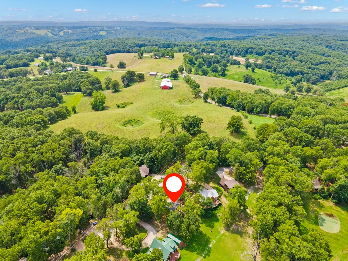 A wide view of expansive green fields dotted with clusters of trees, a red barn, and scattered houses in the distance. The landscape exudes peace and openness, inviting guests and their pets to explore and enjoy the outdoors.